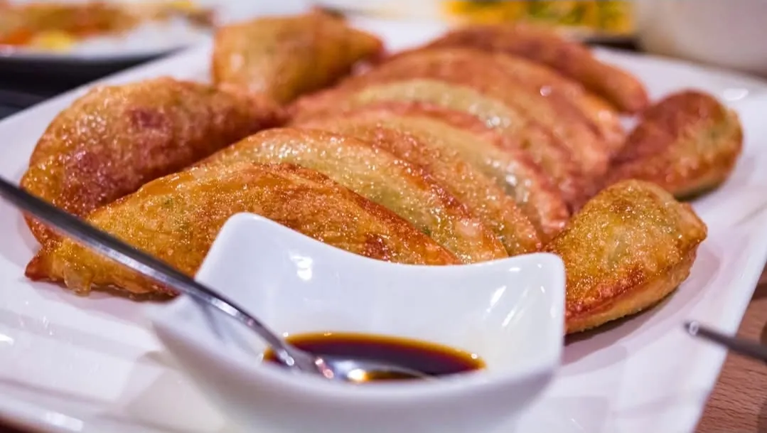 Platte voll knusprig frittierter Mandu-Teigtaschen mit einem geschwungenen Schälchen Sojasauce und Löffel im Vordergrund.