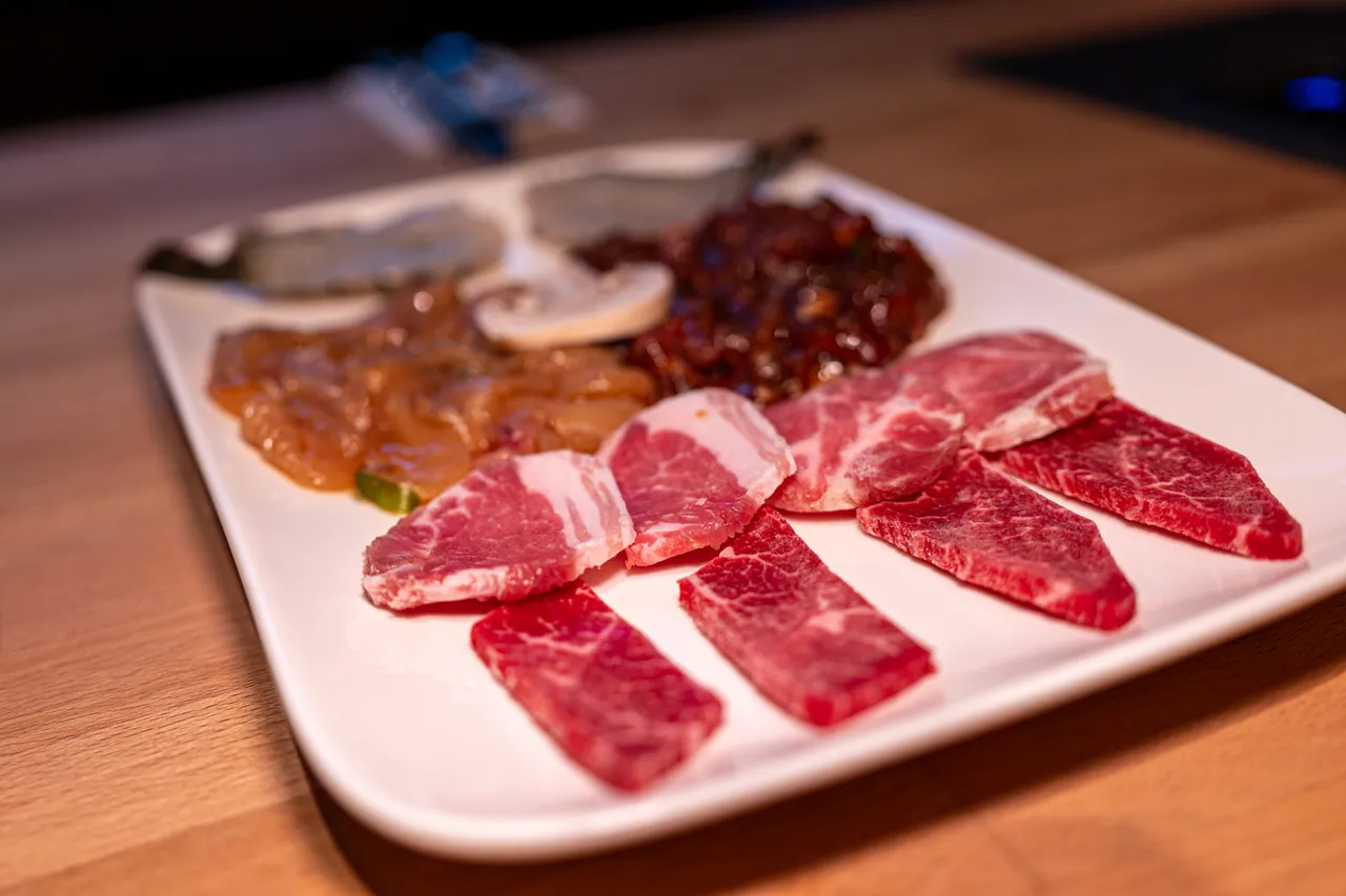 Gemischte Grillplatte mit marmoriertem Rindfleisch, Schweinenackenscheiben, mariniertem hellem Fleisch und dunkel marinierten Fleischwürfeln, garniert mit einem Champignon.