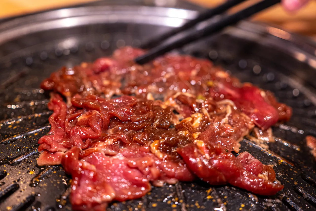Mariniertes Rinderbulgogi brutzelt auf der schwarzen Grillplatte des Tischgrills und wird mit Stäbchen gewendet.